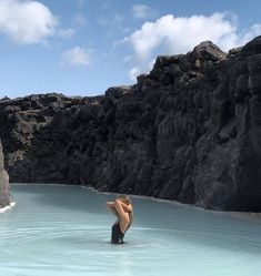 a woman standing in the middle of a body of water with rocks on both sides