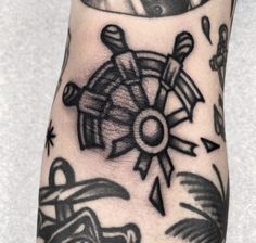 a black and white photo of a hand with tattoos on it's arm, holding a steering wheel