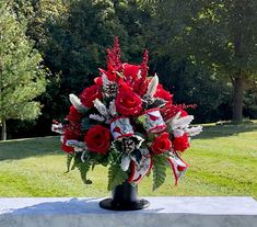 a vase filled with red roses on top of a stone slab in the grass next to trees