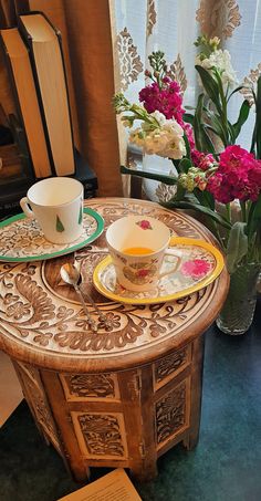 a wooden table topped with a cup and saucer next to a vase filled with flowers