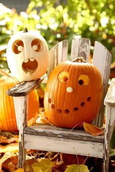 two carved pumpkins sitting on top of a wooden chair in the leaves next to each other