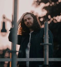 a man with long hair and beard standing next to a metal pole in front of trees