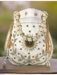 This beautiful Zardosi art work is eye catchy and made of premium material, embellished with Golden Zardosi flower in the center. Material used in this bag is: satin silk, thread, zardosi, sequin, pearl handle. It also boasts of a beautiful Pearl beaded drawstring Tassel. This potli is good match with both Indian and western outfits and are superb for wedding and festive parties. This would be best complement to your designer saree, lehnga or any other kind of dress. This is the combination of t Handwork Embroidered Fabric For Festivals, Bollywood Style Lehenga With Pallu As A Gift, White Embroidered Shoulder Bag For Wedding, Bollywood Style Handwork Pouch As Gift, Elegant Handwork Lehenga For Festivals, Embroidered White Shoulder Bag For Wedding, Bollywood Style Embroidered Pouch Bag, Elegant Lehenga With Pallu As A Gift, Elegant Lehenga With Handwork For Festivals