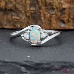 a white opal and diamond ring sitting on top of a black stone table next to a piece of wood