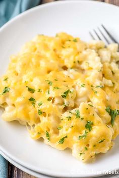 a white plate topped with macaroni and cheese covered in parsley next to a fork