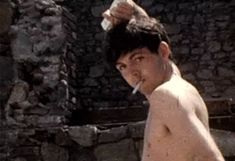 a man with no shirt brushing his hair while standing in front of a stone wall