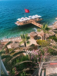 a dock with chairs and umbrellas in the water next to some palm trees,