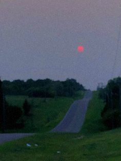 the sun is setting over an empty road and grassy field with power lines on either side