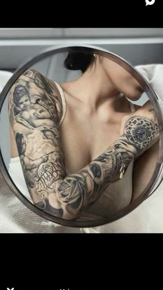 a woman with tattoos on her arm looking in a mirror and holding onto an object