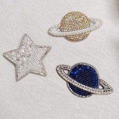 three brooches that are sitting on a white surface, one is blue and the other is gold