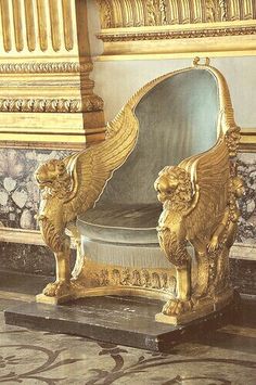 an ornate gold and blue chair with two lions on the arm rests in front of a wall