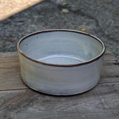 a white and brown bowl sitting on top of a wooden table next to a sidewalk