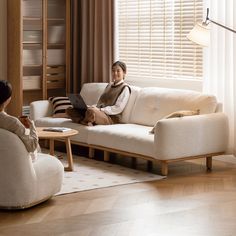 a woman sitting on top of a white couch next to a table with a laptop