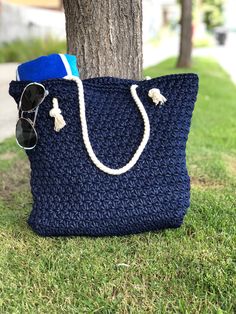 a blue crocheted bag sitting under a tree next to sunglasses and a hat