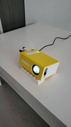 a yellow projector sitting on top of a white table next to a black cord