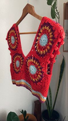 a red crocheted sweater hanging on a wooden hanger next to a potted plant