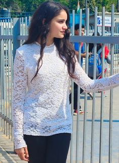 a woman standing in front of a metal fence with her hand on the top of her hip