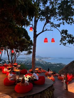 an outdoor dining area overlooking the ocean with red lights hanging from trees and people sitting at tables