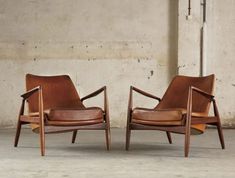 two brown leather chairs sitting next to each other on cement floored area with concrete wall in background