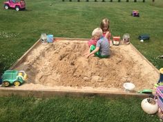 two children playing in a sandbox on the grass