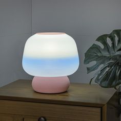 a pink and white lamp sitting on top of a wooden table next to a potted plant