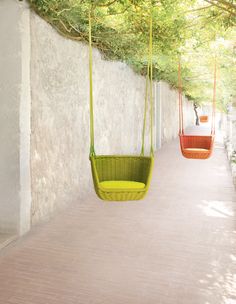 two hanging chairs on the side of a building next to a tree lined sidewalk and walkway