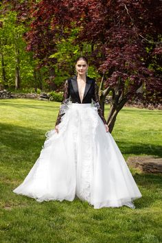 a woman is standing in the grass wearing a white dress and black jacket with sheer sleeves