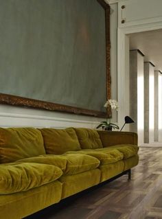 a yellow couch sitting in front of a painting on the wall next to a wooden floor