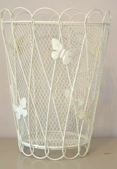 a white wire basket with butterflies on the handles and sides, sitting on a table