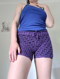 a woman wearing purple shorts and a blue tank top standing in front of a white wall