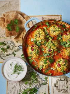 a pan filled with meatballs covered in sauce and garnished with fresh herbs