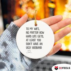 a person holding a white ornament with a quote on it that reads to my wife no matter how hard life gets at least you don't have an ugly husband