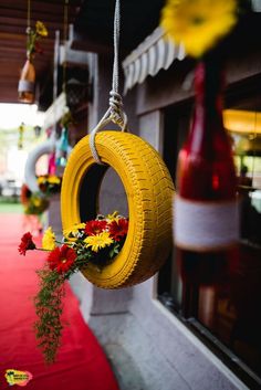 a yellow tire hanging from a rope with flowers in it and red carpet on the ground