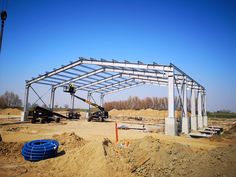 a large metal structure under construction in the middle of a dirt field with blue skies above it