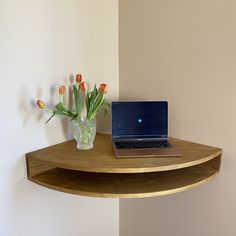 a laptop computer sitting on top of a wooden shelf next to a vase with tulips