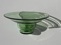 a green glass bowl sitting on top of a white table next to a shadow cast wall