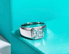 a diamond ring sitting on top of a blue table next to a green box with a white background