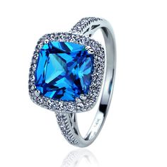 a blue cushion cut ring with diamonds on the sides and an intricate band around it