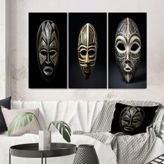 three gold masks on black and white canvases in a living room with a couch