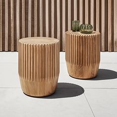 two wooden stools sitting next to each other on a cement floor near a wall