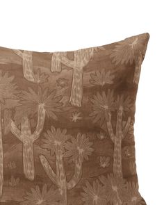 a brown pillow with white flowers and cactus designs on the front, sitting on a white surface