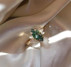 an emerald and diamond ring sitting on top of a white cloth