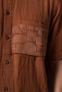 a close up of a person wearing a brown shirt with an embroidered patch on the chest