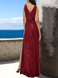 a woman in a long red dress looking out at the ocean with her back to the camera