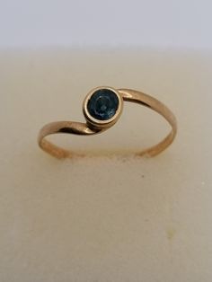 a gold ring with a blue stone in the center on a white surface, ready to be used for jewelry