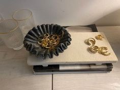 a pair of gold earrings sitting on top of a white tray next to a glass vase