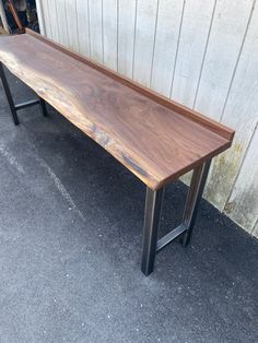 a wooden bench sitting on top of a cement floor next to a building with metal legs