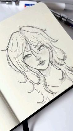 a pencil drawing of a woman's face with long hair and eyes, on top of a notebook