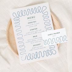 two menu cards sitting on top of a wooden plate next to each other with blue ink