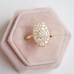 an oval shaped diamond ring sitting on top of a pink velvet box with a gold band